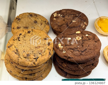 Chocolate chip and cocoa cookies stacked in bakery case. Homemade style, comfort food, and everyday indulgence through classic cookie assortment 136124807