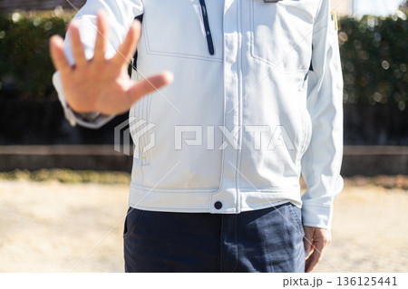 手のひらを見せて拒絶のジェスチャーをしている作業着姿の男性 136125441