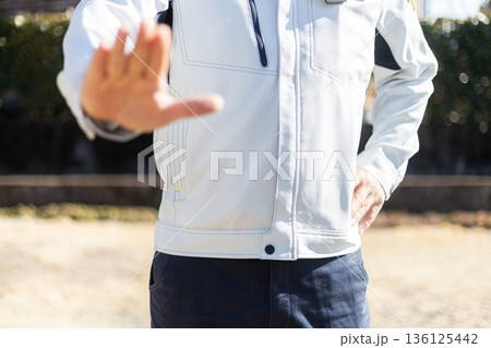 手のひらを見せて拒絶のジェスチャーをしている作業着姿の男性 136125442