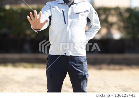 手のひらを見せて拒絶のジェスチャーをしている作業着姿の男性 136125443