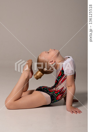 Rhythmic gymnast with cochlear implant stretching on floor in studio. Hearing rehabilitation, body awareness and inclusive childhood flexibility through controlled movement 136125518