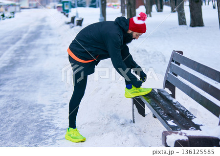 Male runner tying neon sneakers during winter outdoor workout. 136125585