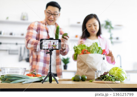 A couple is filming a cooking vlog in their kitchen, showcasing fresh produce and healthy eating habits 136125799