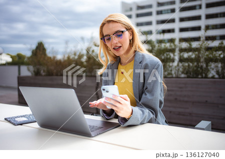Young businesswoman multitasking outdoors with smartphone and laptop Young businesswoman multitasking outdoors with smartphone and laptop 136127040