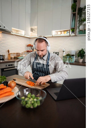 Adult man wearing headphones cooking vegetables in kitchen Adult man wearing headphones cooking vegetables in kitchen 136127155