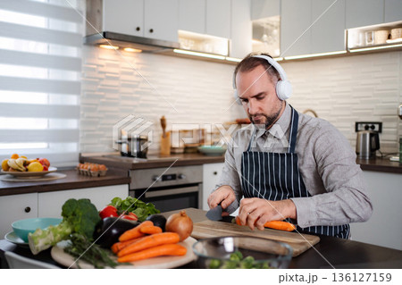 Man wearing headphones preparing healthy food in modern kitchen 136127159