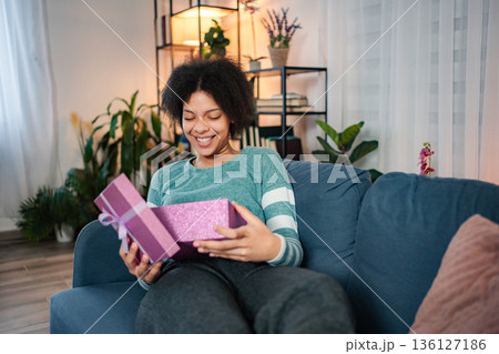 Young woman receiving surprise while opening gift box at home Young woman receiving surprise while opening gift box at home 136127186