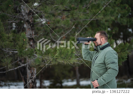 Man birdwatching with binoculars in pine forest during winter Man birdwatching with binoculars in pine forest during winter 136127222