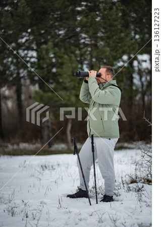Man observing winter forest with binoculars and trekking poles Man observing winter forest with binoculars and trekking poles 136127223