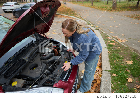 Woman checking car engine in autumn parking lot Woman checking car engine in autumn parking lot 136127319
