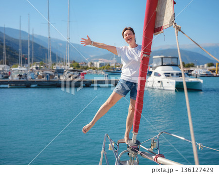 Female sailor holds white sail cloth preparing to hoist sails on yacht. Physical activity and boat handling skills are shown during preparation for sailing trip near Finike coast. Female sailor holds white sail cloth preparing to hoist sails on yacht. Physical activity and boat handling skills are shown during preparation for sailing trip near Finike coast. 136127429