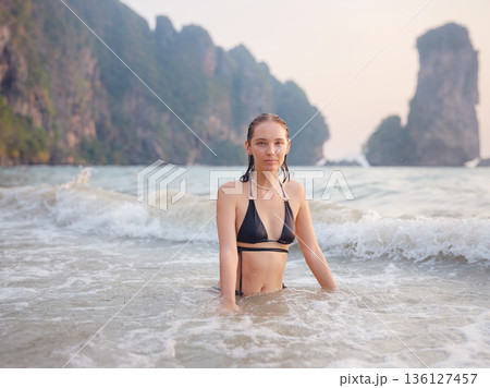 Young woman enjoying serene evening at sea in Krabi, Thailand during sunset. Calm waves, golden light, and peaceful atmosphere highlight tropical beauty and connection with nature. Young woman enjoying serene evening at sea in Krabi, Thailand during sunset. Calm waves, golden light, and peaceful atmosphere highlight tropical beauty and connection with nature. 136127457