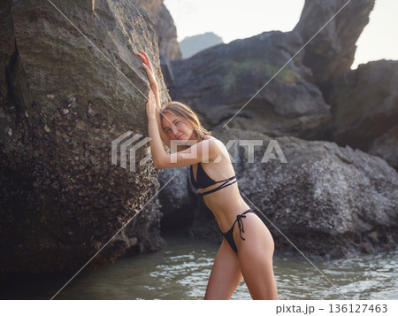 Young woman enjoying serene evening at sea in Krabi, Thailand during sunset. Calm waves, golden light, and peaceful atmosphere highlight tropical beauty and connection with nature. Young woman enjoying serene evening at sea in Krabi, Thailand during sunset. Calm waves, golden light, and peaceful atmosphere highlight tropical beauty and connection with nature. 136127463