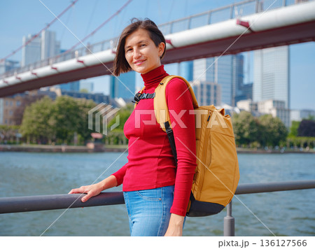 Tourist woman explores modern Frankfurt, walking through vibrant streets with contemporary architecture, skyscrapers, and urban spaces, enjoying lively atmosphere of modern side. Tourist woman explores modern Frankfurt, walking through vibrant streets with contemporary architecture, skyscrapers, and urban spaces, enjoying lively atmosphere of modern side. 136127566
