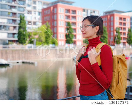 Tourist woman explores modern Frankfurt, walking through vibrant streets with contemporary architecture, skyscrapers, and urban spaces, enjoying lively atmosphere of modern side. 136127571