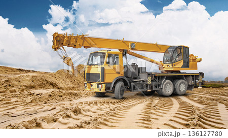 A truck crane is ready for work at a construction site. A large pile of sand is visible in the background, indicating ongoing construction work A truck crane is ready for work at a construction site. A large pile of sand is visible in the background, indicating ongoing construction work 136127780