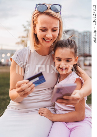 Mother and daughter shopping online using a credit card and a smartphone Mother and daughter shopping online using a credit card and a smartphone 136127812