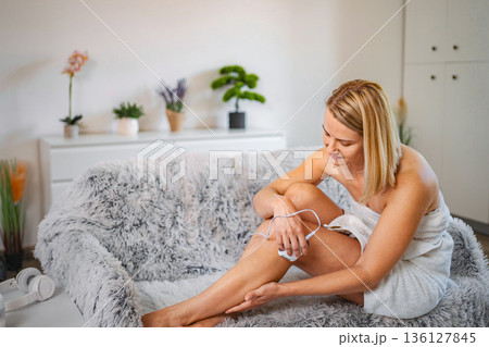Woman removing leg hair with an electric epilator at home Woman removing leg hair with an electric epilator at home 136127845