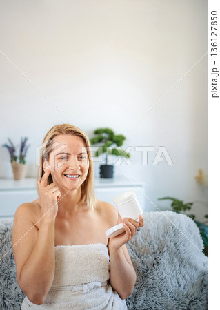 Smiling woman applying face cream at home 136127850