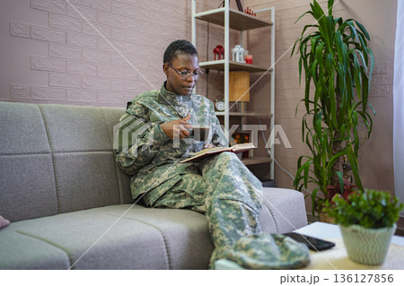Soldier relaxing at home reading a book and drinking coffee 136127856