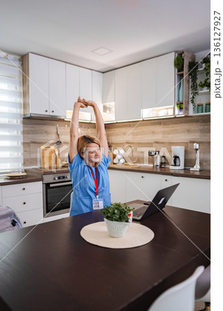 Female Doctor Stretching in her Kitchen after Online Meeting 136127927