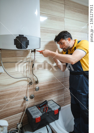 Plumber fixing a water heater in a bathroom using pliers Plumber fixing a water heater in a bathroom using pliers 136127931
