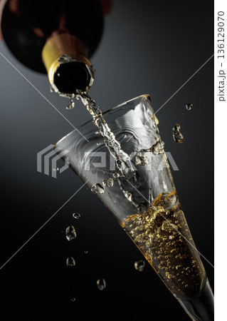 White sparkling wine is poured from a bottle into a glass. White sparkling wine is poured from a bottle into a glass. 136129070