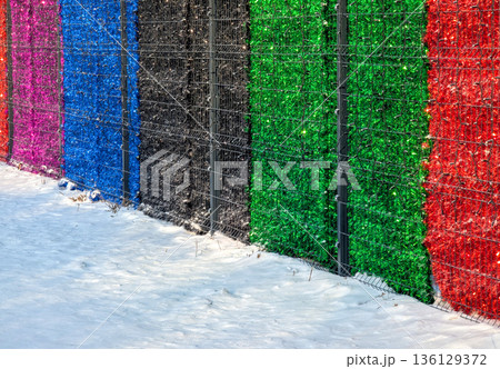Decorative tinsel panels with bold colors line winter alleyway scene. Vibrant tinsel decorations featuring vivid colors and metallic shine create festive mood in city alley 136129372