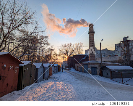 Urban winter landscape. Morning scene of snowy alley. Frozen alley with rusted doors and cloudy sky. Chilly city street with snowy ground and fading orange dawn 136129381