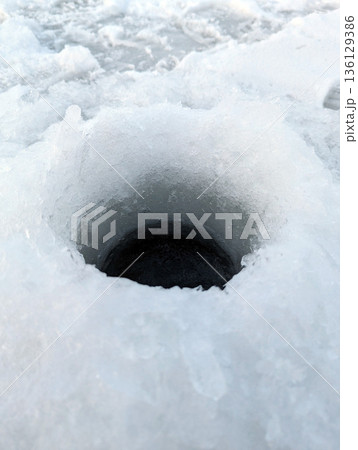 A perfectly round fishing hole cut into the thick ice of a frozen river. A perfectly round fishing hole cut into the thick ice of a frozen river. 136129386