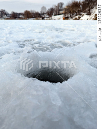 Traditional winter fishing spot with a small hole in the ice and slush. Traditional winter fishing spot with a small hole in the ice and slush. 136129387