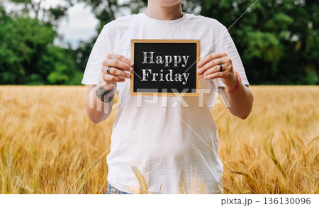 Person holding a chalkboard sign with a cheerful message in a golden wheat field 136130096