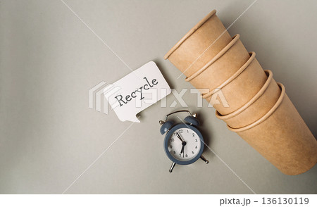 Clock sits on a table next to a stack of paper cups 136130119