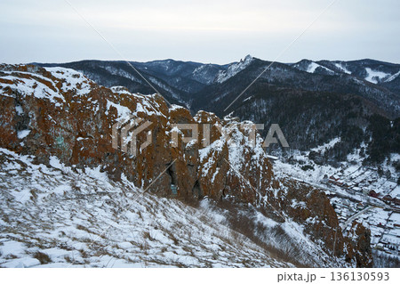 Snowy mountain landscape with rocky cliffs and a village nestled in the valley below, showcasing winter nature. 136130593