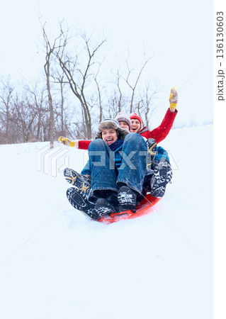Young people sledding together downhill in snowy park Young people sledding together downhill in snowy park 136130603