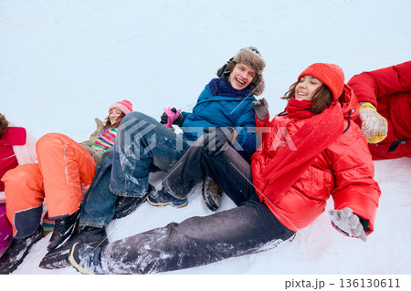 Laughing friends sitting on snow after winter sledding fun. Laughing friends sitting on snow after winter sledding fun. 136130611
