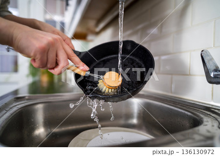 Woman washing a frying pan in the kitchen with eco friendly wooden brush for sustainable lifestyle Woman washing a frying pan in the kitchen with eco friendly wooden brush for sustainable lifestyle 136130972