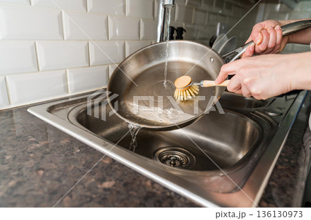 Woman washing a frying pan in the kitchen with eco friendly wooden brush for sustainable lifestyle 136130973