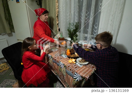 Family gathers around a table laden with food and drink, sharing a meal together. 136131169