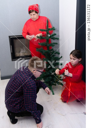 Family decorating a small artificial Christmas tree together, enjoying the holiday season. Family decorating a small artificial Christmas tree together, enjoying the holiday season. 136131172