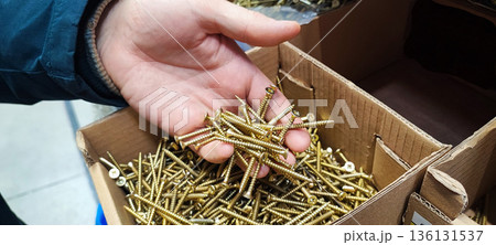 A man's hand picking up a handful of metal nails from a cardboard box at a hardware store or warehouse. Concept art of handicrafts, building materials, craftsmanship, and industrial supplies. 136131537