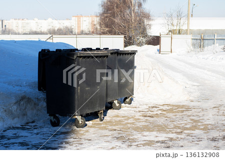 Municipal waste containers stand on frozen ground under winter sunlight near apartment complexes Municipal waste containers stand on frozen ground under winter sunlight near apartment complexes 136132908