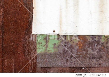 Front view of a rusted metal wall with peeling paint, layered green and brown panels 136132983
