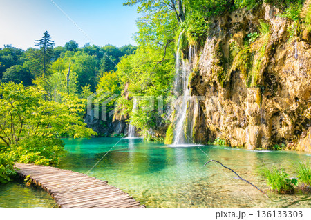Wooden footpath at Plitvice national park, Croatia. Pathway in the forest near the lake and waterfall. Fresh beautiful nature, peaceful place. Famous tourist destination. Wooden footpath at Plitvice national park, Croatia. Pathway in the forest near the lake and waterfall. Fresh beautiful nature, peaceful place. Famous tourist destination. 136133303