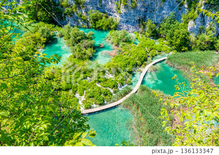 Aerial view of wooden footpath trail at Plitvice lakes, Croatia. Tourist path above blue lagoon near the waterfalls. Empty bridge without peoples. Aerial view of wooden footpath trail at Plitvice lakes, Croatia. Tourist path above blue lagoon near the waterfalls. Empty bridge without peoples. 136133347