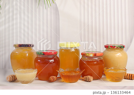 Variety of honey varieties in jars and cups on the kitchen table.Assortment of meadow, lime, flower, bee honey and nectar for banner at honey fair or sale, natural healthy product for health Variety of honey varieties in jars and cups on the kitchen table.Assortment of meadow, lime, flower, bee honey and nectar for banner at honey fair or sale, natural healthy product for health 136133464
