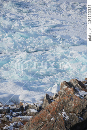 Cracked turquoise ice plates cover the frozen surface of Lake Baikal beside rugged rocks, forming layered winter textures in cold daylight Cracked turquoise ice plates cover the frozen surface of Lake Baikal beside rugged rocks, forming layered winter textures in cold daylight 136133525