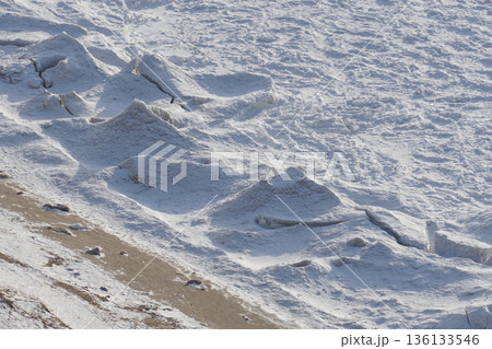 Frozen wave formations line the shoreline of Lake Baikal, creating sculpted ice ridges and textured snow under cold daylight Frozen wave formations line the shoreline of Lake Baikal, creating sculpted ice ridges and textured snow under cold daylight 136133546