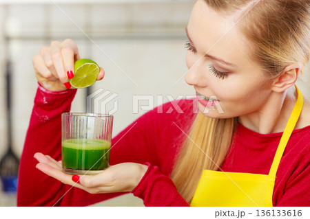 Woman in kitchen holding vegetable smoothie juice Woman in kitchen holding vegetable smoothie juice 136133616