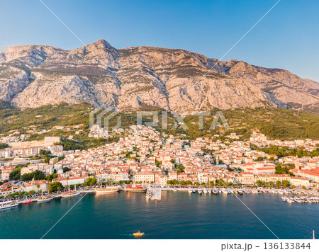 Drone aerial view of Makarska city, Croatia. Sunset over the city, beach and se. Biokovo mountains in the background. Summer time. Drone aerial view of Makarska city, Croatia. Sunset over the city, beach and se. Biokovo mountains in the background. Summer time. 136133844